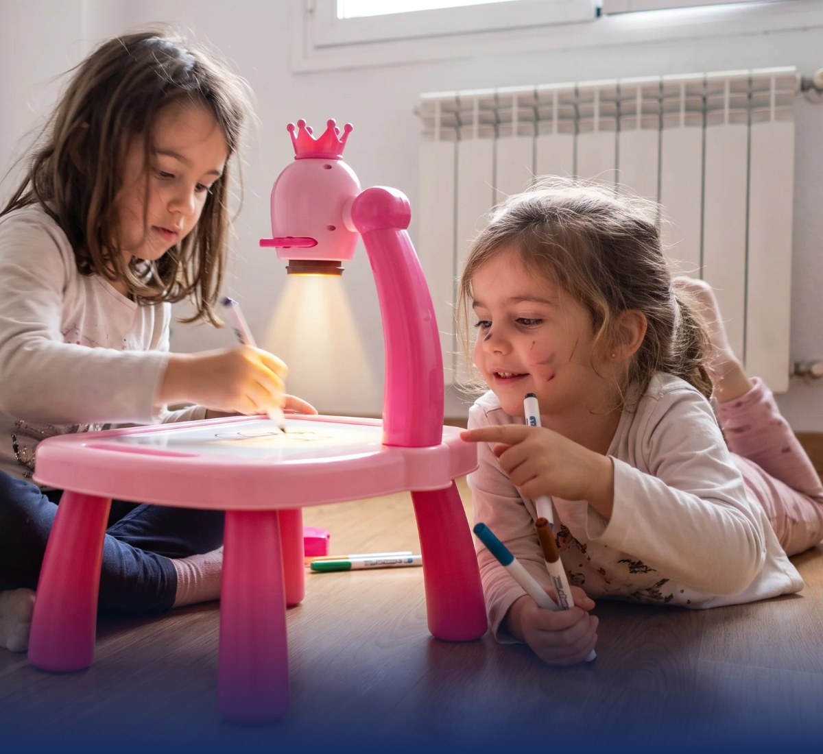 Dos niñas dibujando juntas en la mesita con proyector rosa